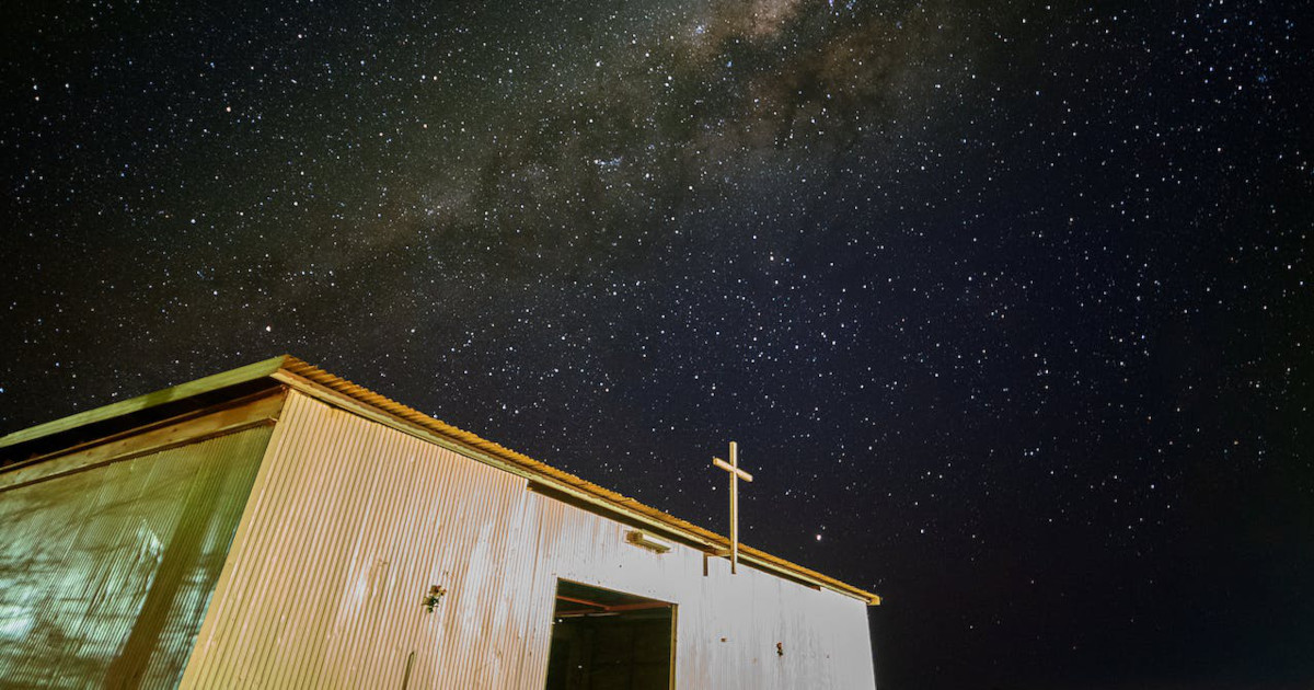 A humble building with a cross atop, beneath a starry night sky