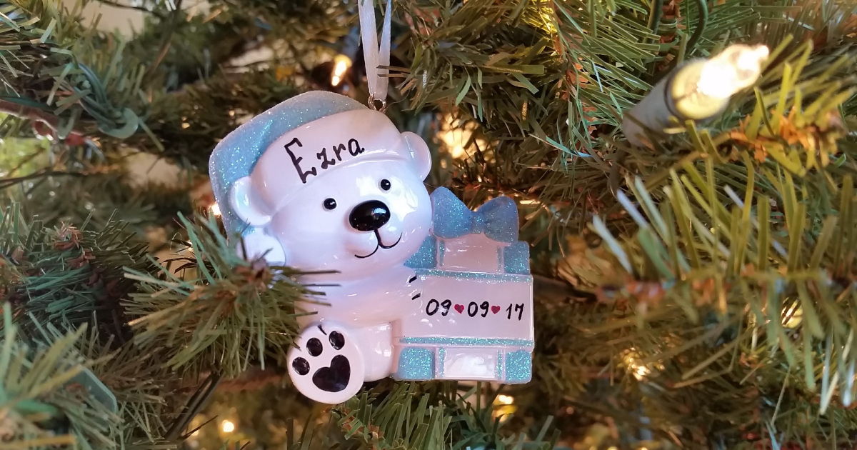A polar bear ornament with the name Ezra written on it, hanging on a Christmas tree