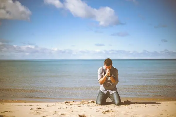 A man kneeling on the beach to pray